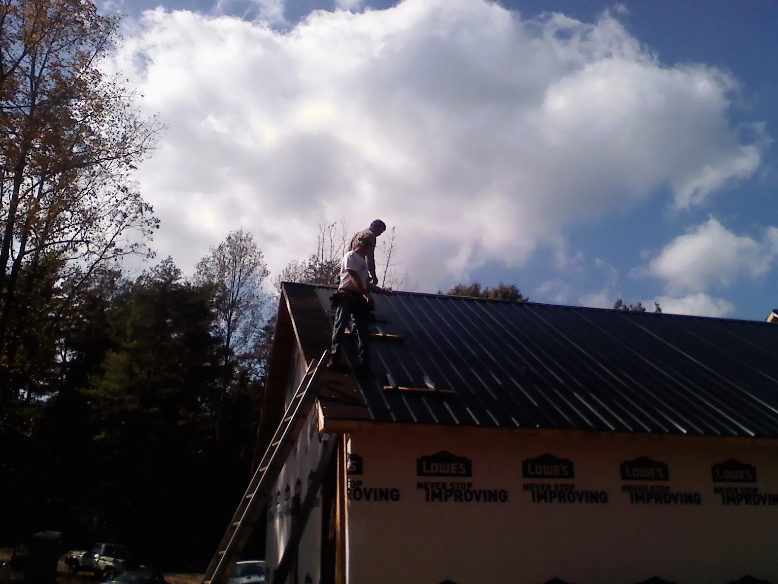 Roofer fastening dark metal panels high against a cloudy sky, from a Roof Inspection job in Zillah
