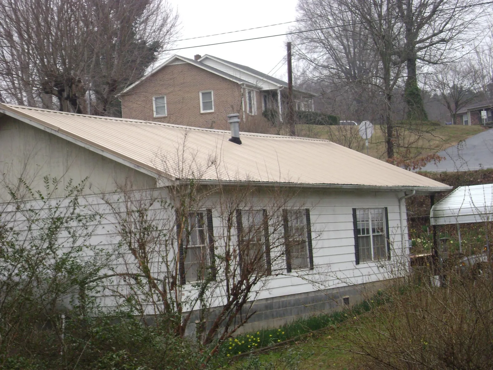 Tan metal roof on a white sided house set into a hillside — Commercial Roofing by Roofing Brothers in Zillah